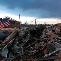 An American flag blows in the wind at sunrise atop the rubble of a destroyed home in Moore, Okla., on May 21, 2013, a day after a tornado roared through the Oklahoma City suburb, flattening entire neighborhoods and destroying an elementary school with a direct blow as children and teachers huddled against winds up to 200 mph. (Brennan Linsley/AP Photo)